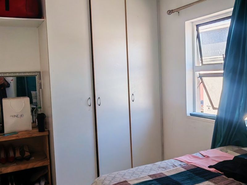 A bedroom featuring built-in white cupboards, tiled flooring, and a window with a curtain rod, offering a functional space with potential for cosmetic updates.