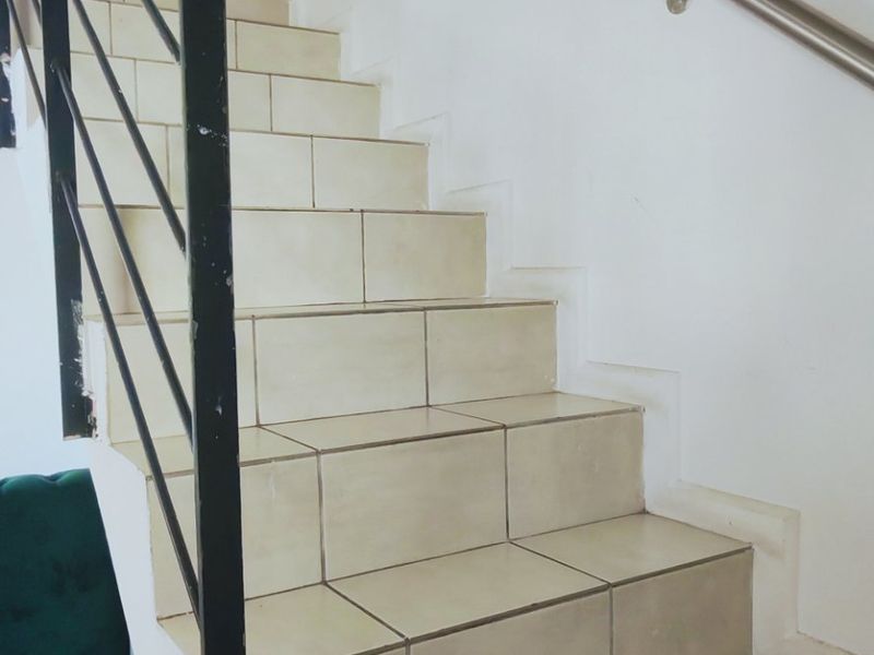 A functional staircase featuring tiled steps, a metal balustrade, and a wall-mounted handrail, showing signs of wear on the metal fixtures.