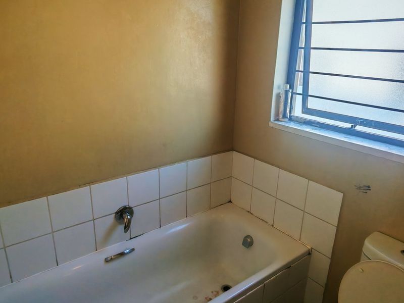 A compact bathroom featuring a standard bathtub, toilet, and security bars on the window, requiring cosmetic updates to the wall finishes.