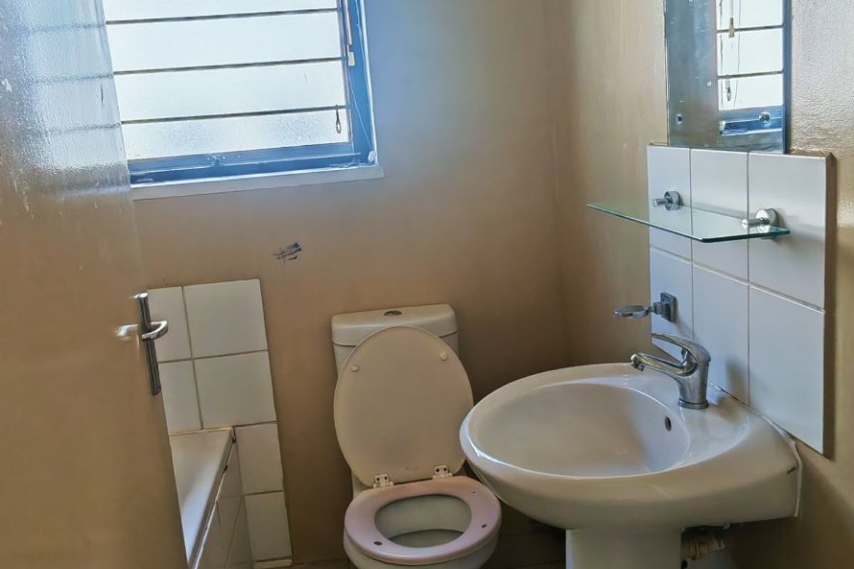 A functional bathroom featuring a pedestal basin, toilet, and bathtub with tiled flooring and wall-mounted mirror, requiring cosmetic updates to improve its condition.