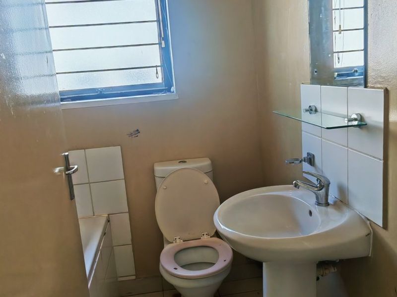 A functional bathroom featuring a pedestal basin, toilet, and bathtub with tiled flooring and wall-mounted mirror, requiring cosmetic updates to improve its condition.