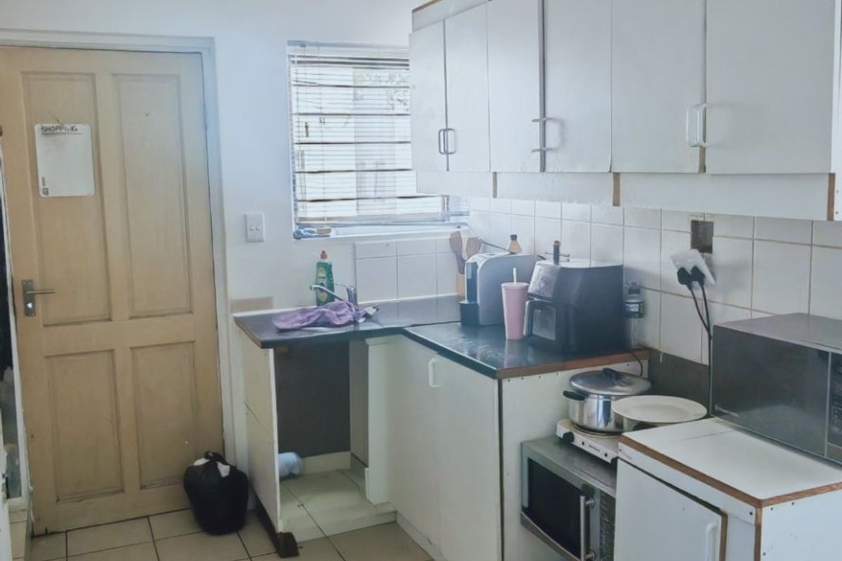 A functional kitchen featuring white built-in cabinetry, tiled backsplash, and tiled flooring, offering a practical layout with potential for modern updates.