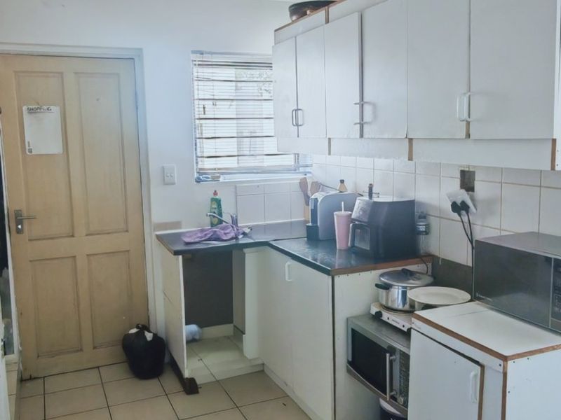 A functional kitchen featuring white built-in cabinetry, tiled backsplash, and tiled flooring, offering a practical layout with potential for modern updates.