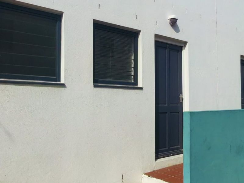 Exterior view of the apartment entrance featuring paved access, tiled steps, and secure door entry with modern aluminium window frames.