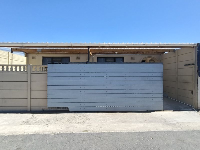 Front elevation of the property featuring a concrete driveway, a covered carport area, and a privacy gate with boundary walling.