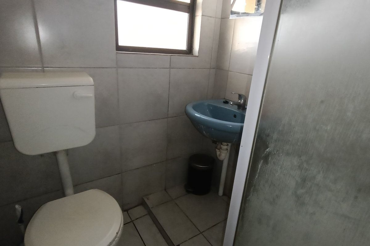 A compact bathroom featuring tiled walls and flooring, a standard toilet, a wall-mounted basin, and a shower enclosure.