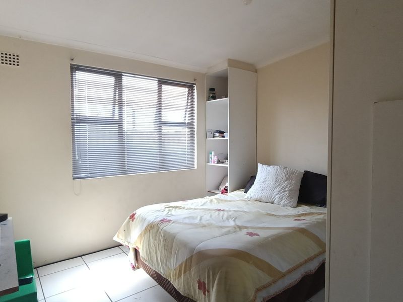 A functional bedroom featuring tiled flooring, built-in shelving, and a window with venetian blinds, offering a neutral base for potential updates.