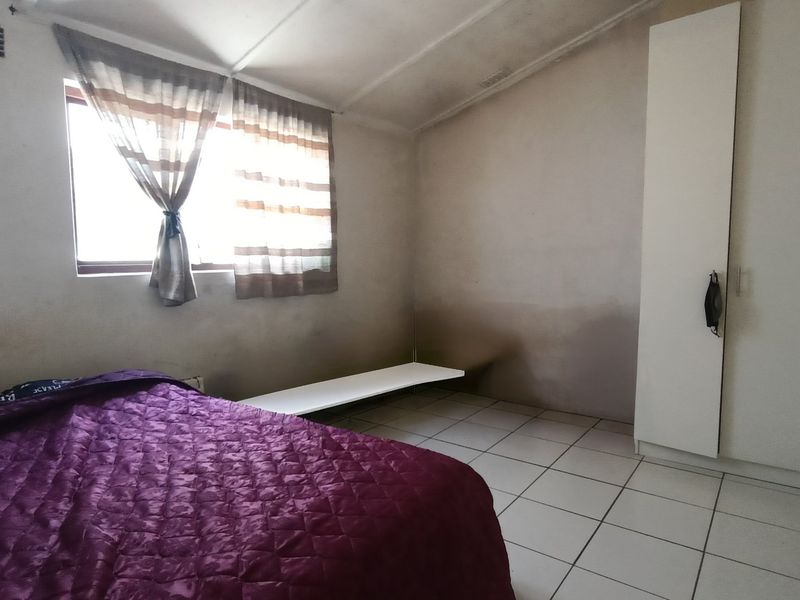 A bedroom featuring tiled flooring and a built-in wardrobe, currently showing visible signs of wall staining and dampness requiring attention.