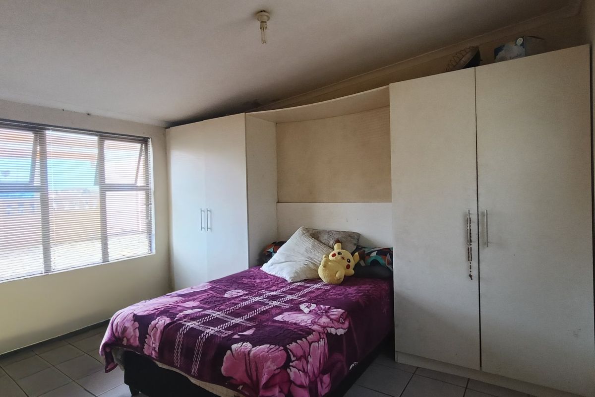 A bedroom featuring built-in cupboards, tiled flooring, and natural light from aluminium-framed windows.