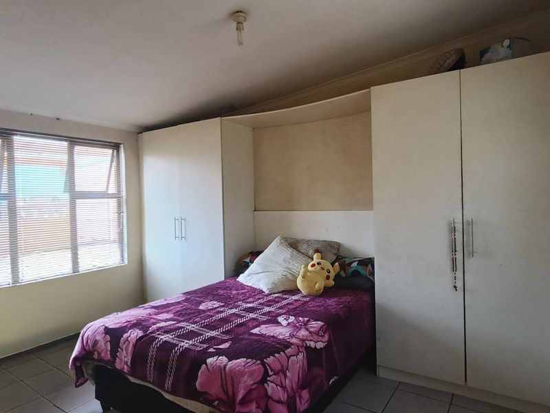 A bedroom featuring built-in cupboards, tiled flooring, and natural light from aluminium-framed windows.