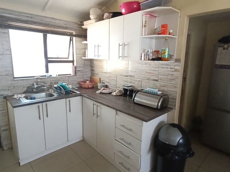 A functional kitchen featuring white cabinetry, laminate countertops, a stainless steel sink, and a tiled backsplash with neutral floor tiles.