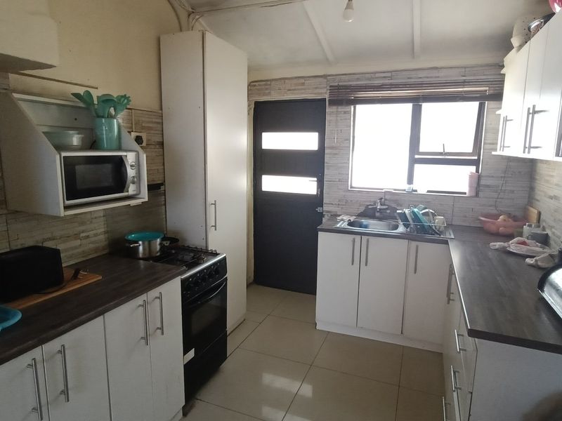 Functional kitchen featuring white cabinetry, dark laminate countertops, gas stove, and tiled backsplash with direct access to the exterior.