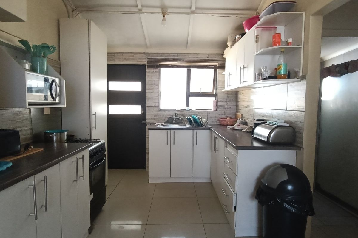 A functional kitchen featuring white cabinetry, laminate countertops, tiled flooring, and a tiled backsplash, providing a practical workspace with direct exterior access.