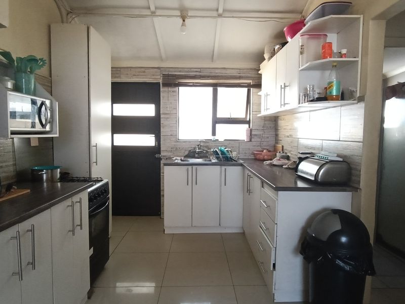 A functional kitchen featuring white cabinetry, laminate countertops, tiled flooring, and a tiled backsplash, providing a practical workspace with direct exterior access.