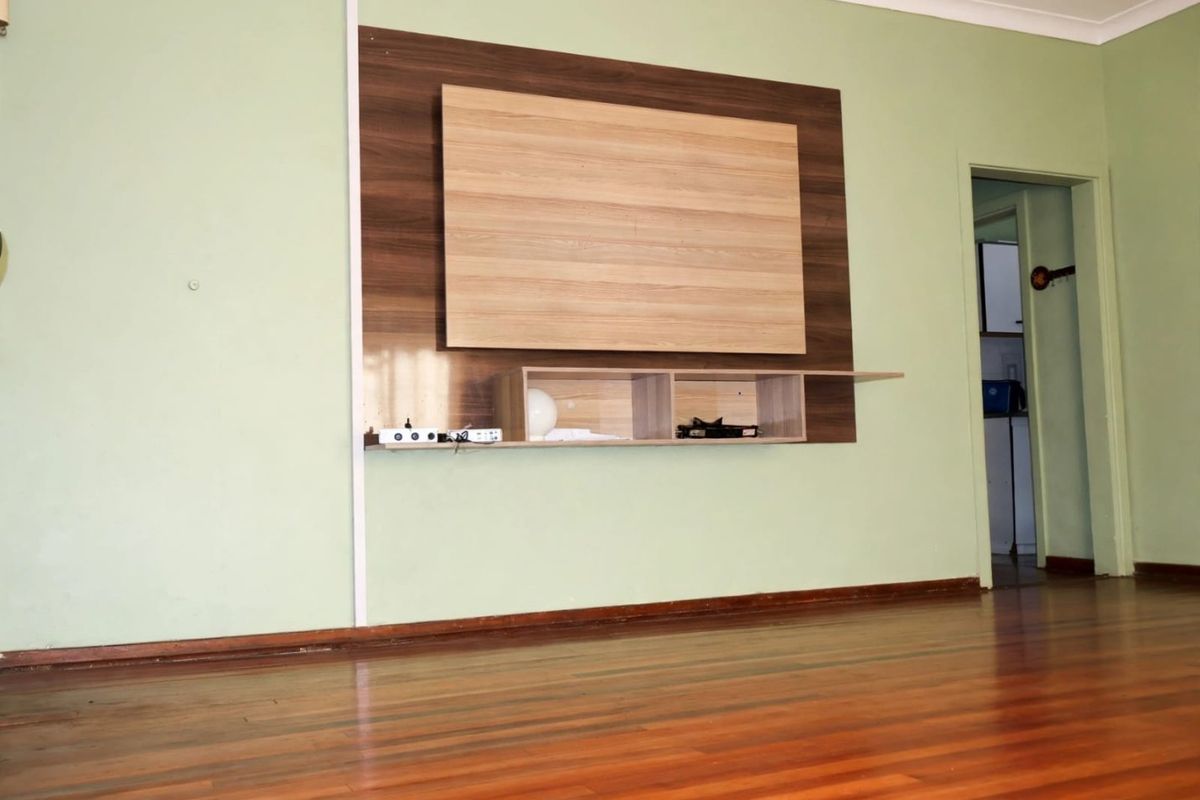 A spacious living room featuring polished timber flooring and a built-in wall-mounted media console unit.