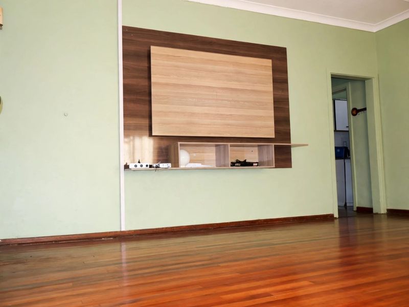 A spacious living room featuring polished timber flooring and a built-in wall-mounted media console unit.
