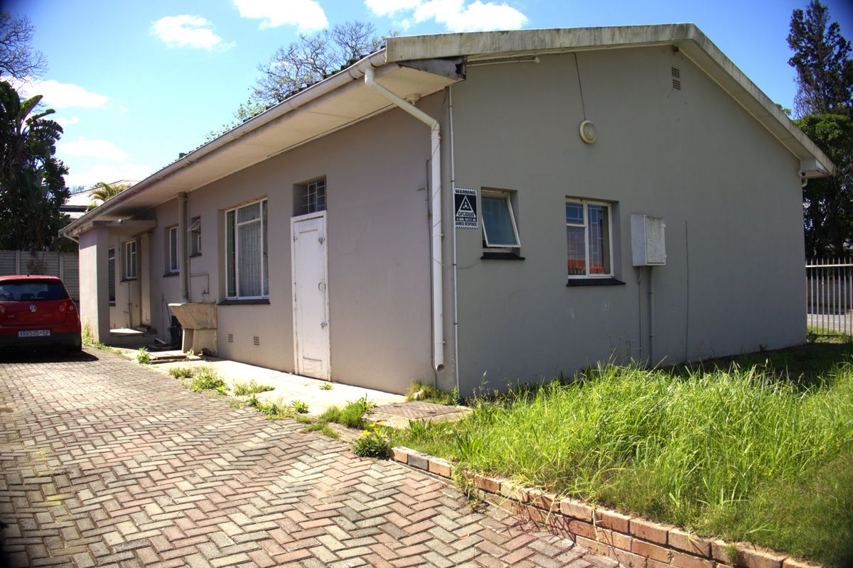 Rear exterior view of the property featuring a paved driveway, external utility sink, and basic building facade with visible maintenance requirements.