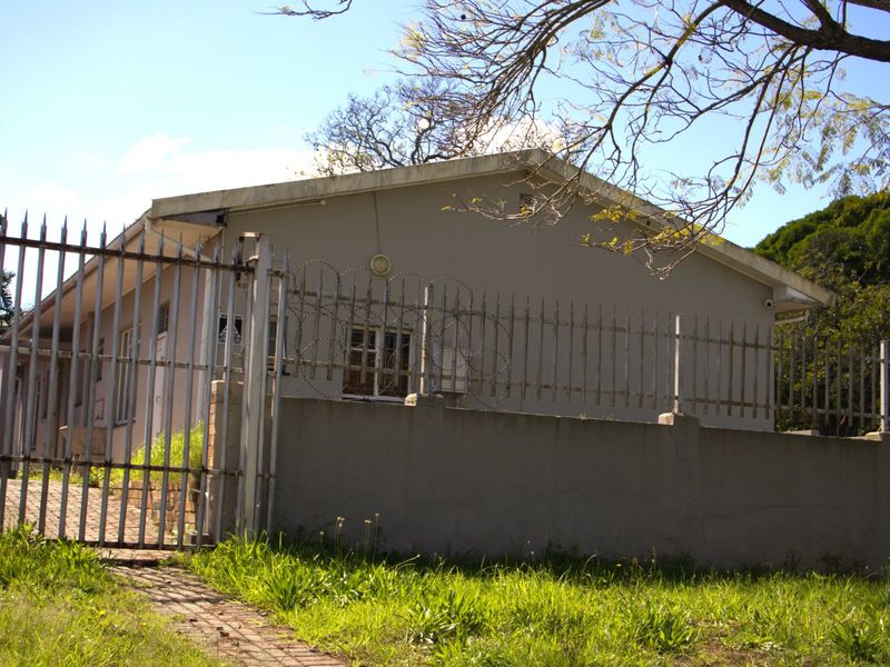 Front exterior view of the property featuring a paved driveway, concrete boundary wall, and metal security fencing with razor wire.