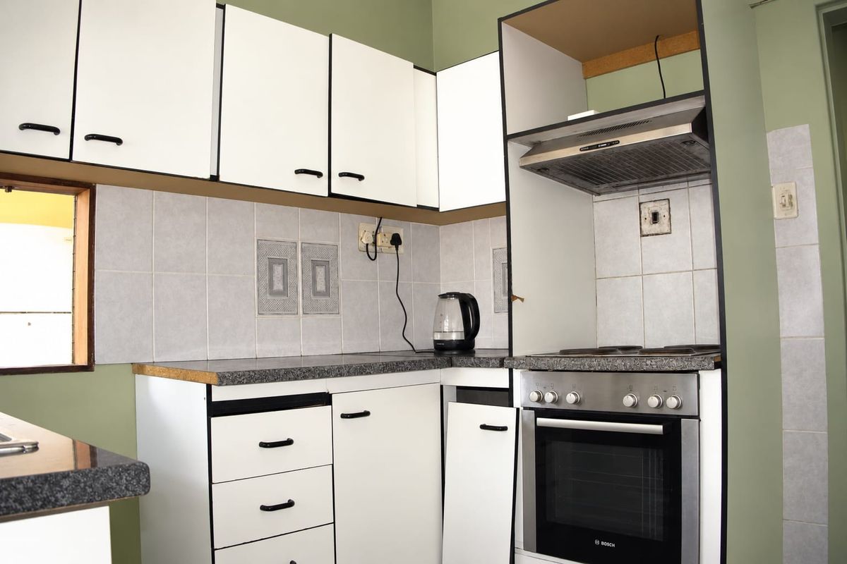 A compact kitchen featuring white cabinetry, tiled backsplash, and built-in oven with hob, currently showing signs of wear and missing cabinet hardware.