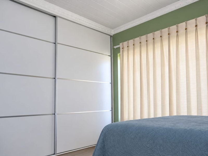 A well-maintained bedroom featuring a large built-in sliding door wardrobe, decorative crown molding, and a classic tongue and groove ceiling finish.