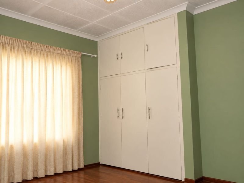 A clean, empty bedroom featuring timber flooring, green painted walls, and ample built-in cupboard storage space.