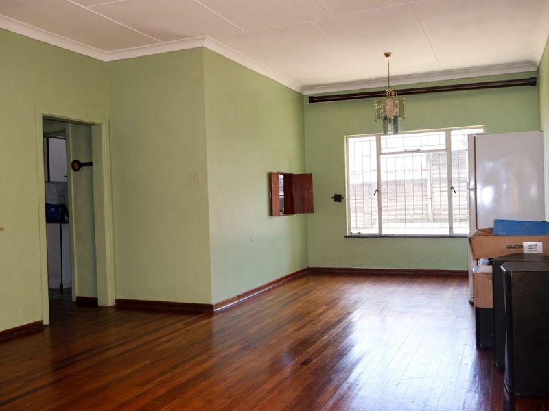 An empty living room featuring original hardwood flooring, green painted walls, and a window with security bars.