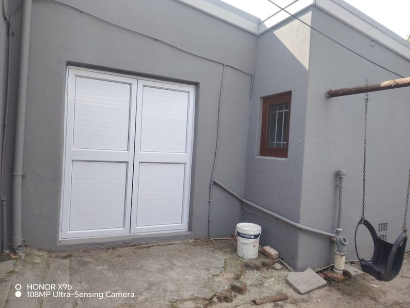 Rear exterior view showing a concrete patio area with double aluminium doors and a small window with security bars.