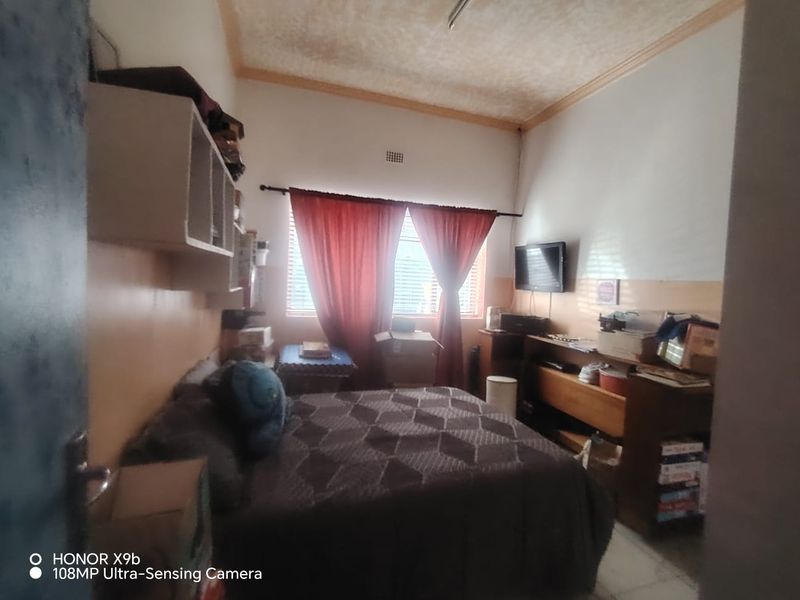 A bedroom featuring built-in shelving and ceiling cornice, currently showing signs of wear and dated finishes that would benefit from cosmetic updates.