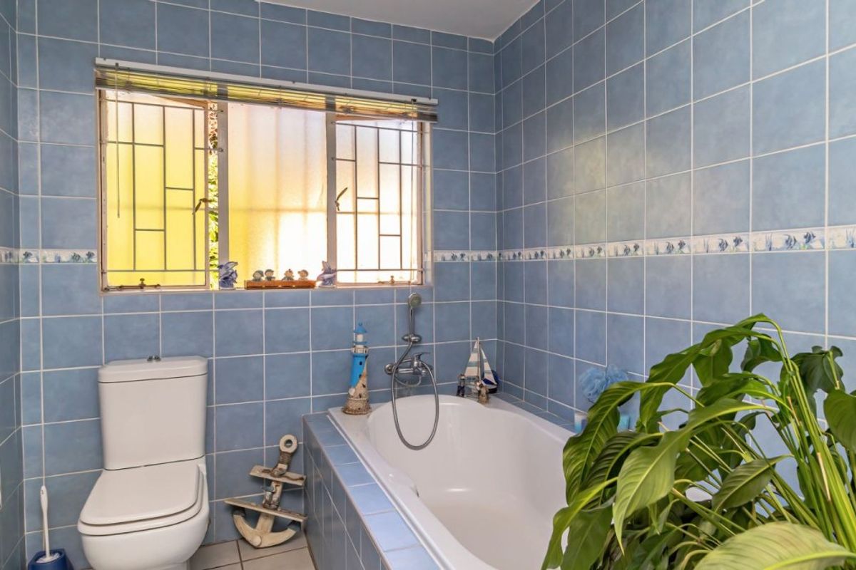 A functional bathroom featuring a built-in bathtub, toilet, and blue wall tiling with a window providing natural light.