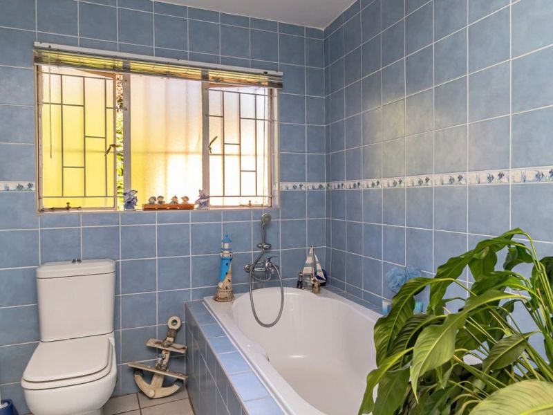 A functional bathroom featuring a built-in bathtub, toilet, and blue wall tiling with a window providing natural light.