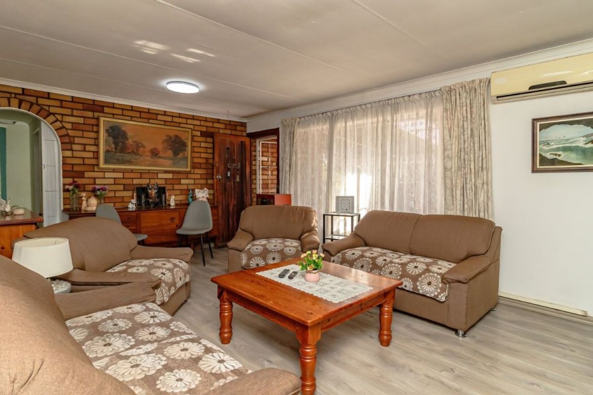 A comfortable living room featuring a rustic brick accent wall, laminate flooring, and a wall-mounted split-system air conditioner for climate control.