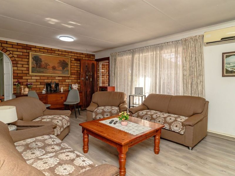 A comfortable living room featuring a rustic brick accent wall, laminate flooring, and a wall-mounted split-system air conditioner for climate control.