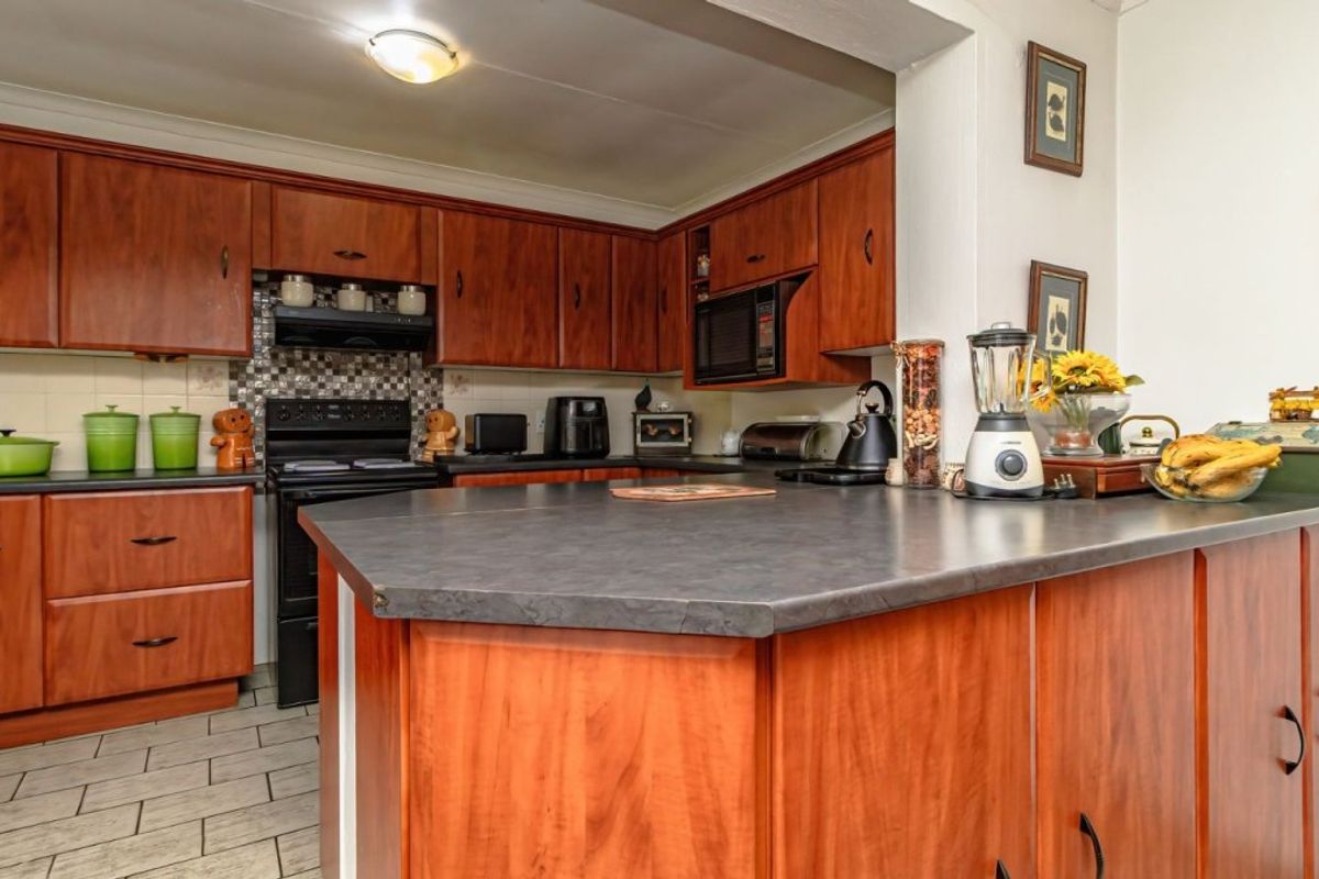 A functional kitchen featuring wood-tone cabinetry, dark laminate countertops, a built-in oven, and a tiled backsplash, offering a classic layout with ample storage space.
