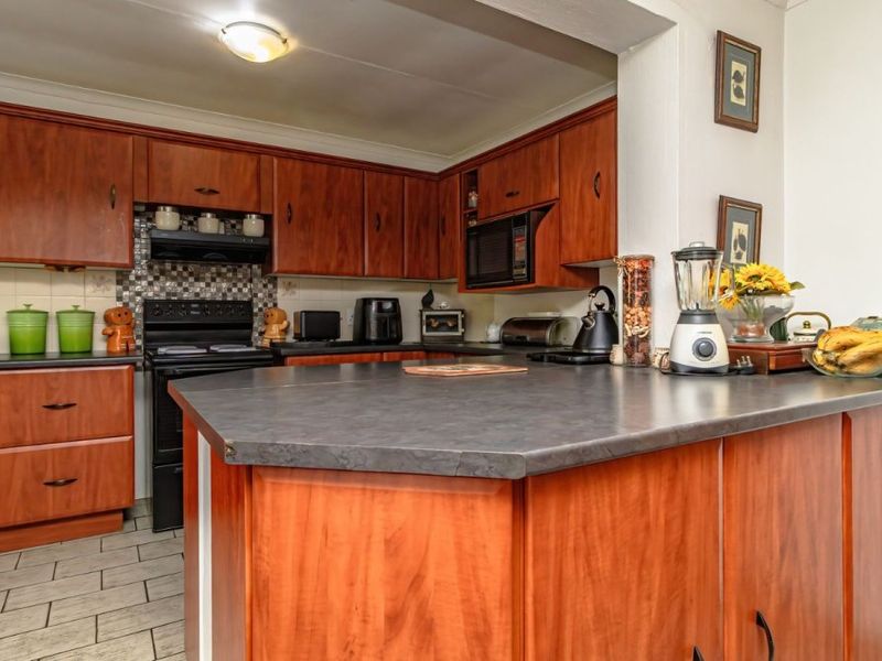 A functional kitchen featuring wood-tone cabinetry, dark laminate countertops, a built-in oven, and a tiled backsplash, offering a classic layout with ample storage space.