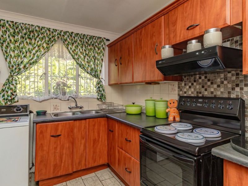 A functional kitchen featuring wood-look cabinetry, dark laminate countertops, a mosaic tile backsplash, and a freestanding oven with an integrated extractor fan.