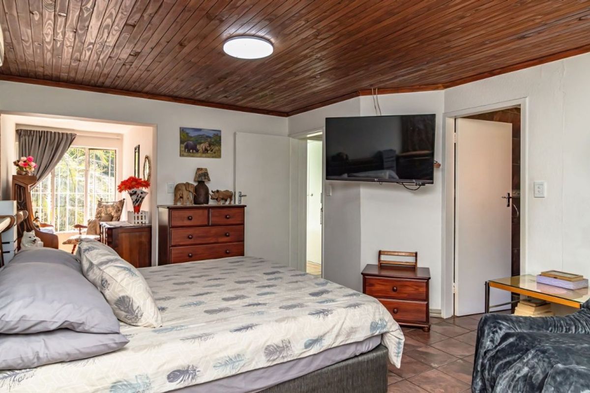 Spacious bedroom featuring a warm timber-clad ceiling, tiled flooring, and direct access to an adjoining sunroom area.