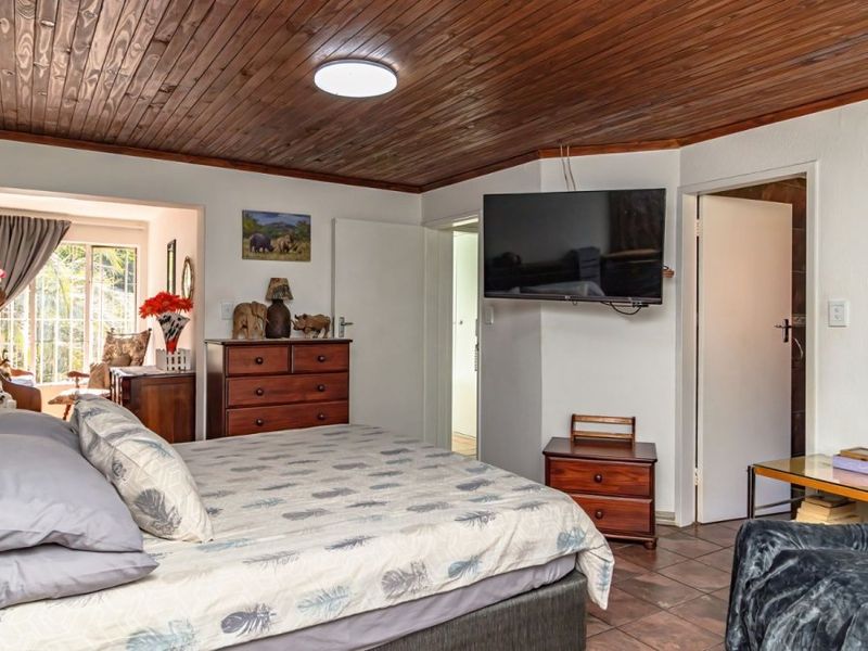 Spacious bedroom featuring a warm timber-clad ceiling, tiled flooring, and direct access to an adjoining sunroom area.