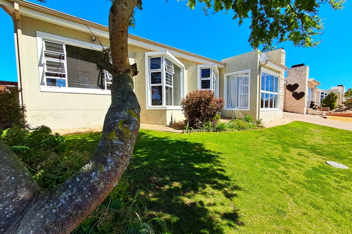 Rear view of the house featuring a well-maintained lawn, paved walkway, bay windows, and a stone-clad chimney.