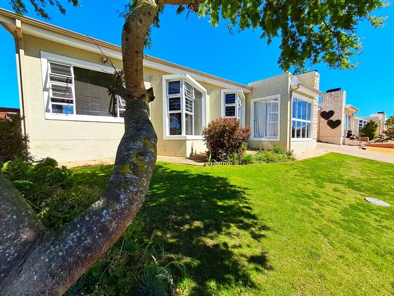 Rear view of the house featuring a well-maintained lawn, paved walkway, bay windows, and a stone-clad chimney.