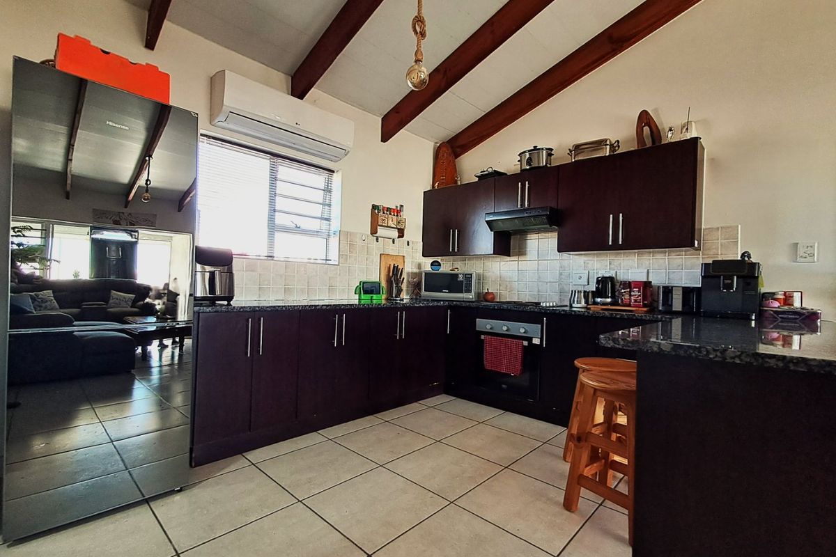 A functional kitchen featuring dark wood cabinetry, granite countertops, tiled backsplash, and exposed timber ceiling beams, complemented by tiled flooring and an integrated air conditioner.