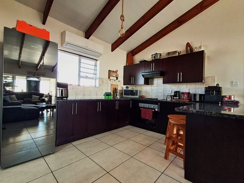 A functional kitchen featuring dark wood cabinetry, granite countertops, tiled backsplash, and exposed timber ceiling beams, complemented by tiled flooring and an integrated air conditioner.