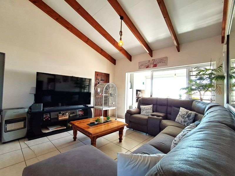 Spacious living room featuring high vaulted ceilings with exposed timber beams, tiled flooring, and large sliding glass doors providing access to the outdoor area.