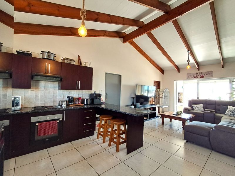 Spacious open-plan living area featuring a kitchen with granite countertops, built-in appliances, and a vaulted ceiling with exposed timber beams leading to a patio.