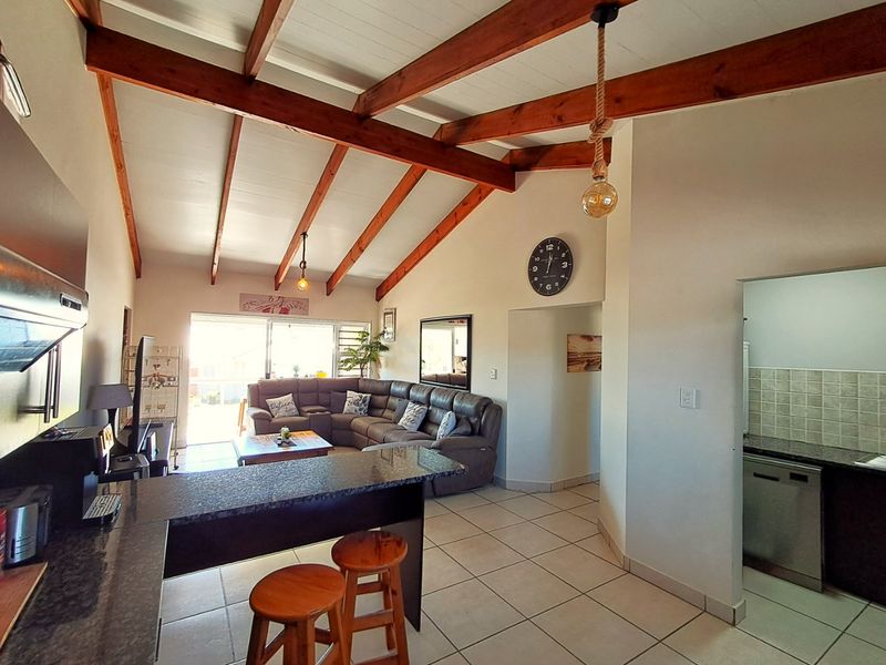 Spacious open-plan living area featuring exposed timber beams, tiled flooring, and a functional kitchen with granite countertops and direct access to the patio.