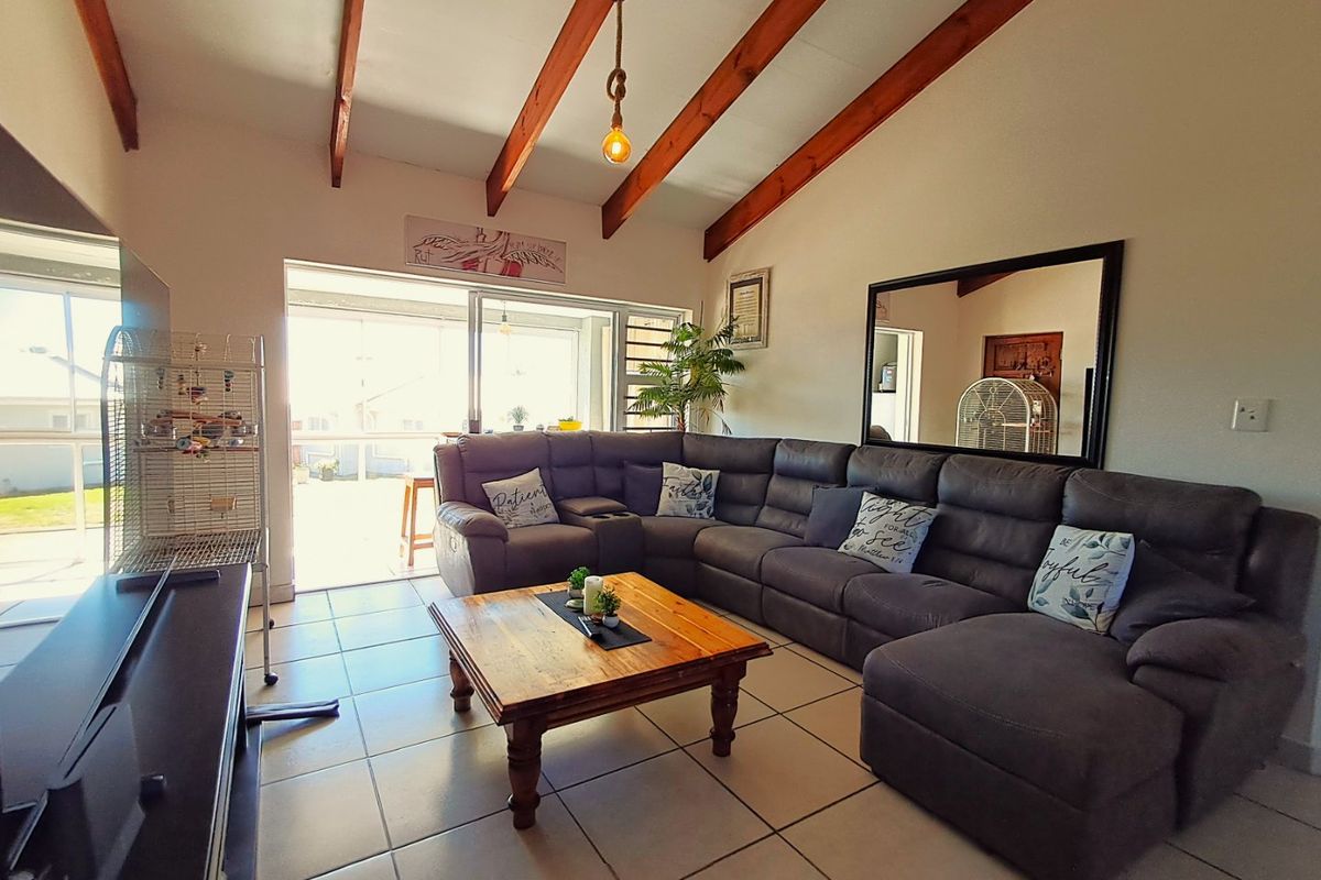 Spacious living room featuring a vaulted ceiling with exposed timber beams, ceramic tiled flooring, and large sliding glass doors leading to an outdoor area.