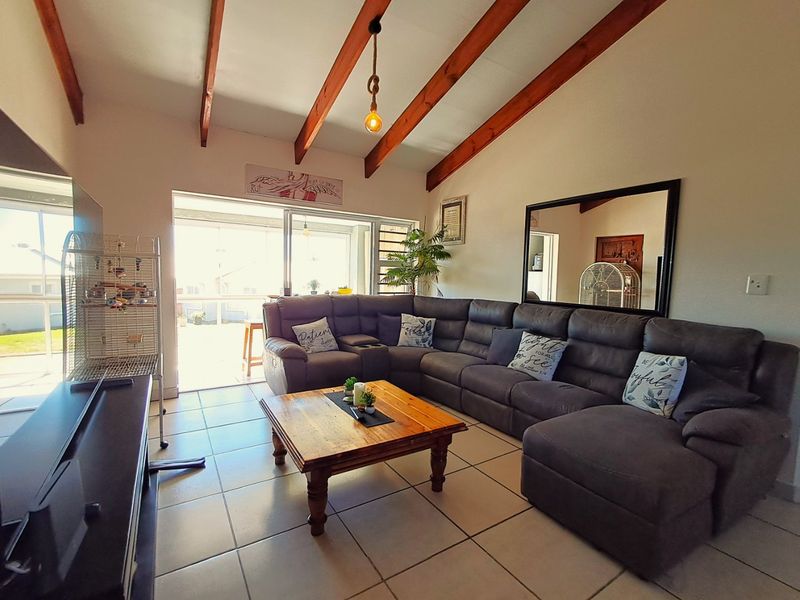 Spacious living room featuring a vaulted ceiling with exposed timber beams, ceramic tiled flooring, and large sliding glass doors leading to an outdoor area.
