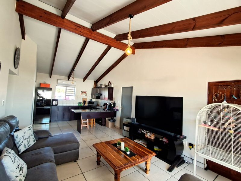 Spacious open-plan living area featuring vaulted ceilings with exposed timber beams, tiled flooring, and a functional kitchen with a central island.