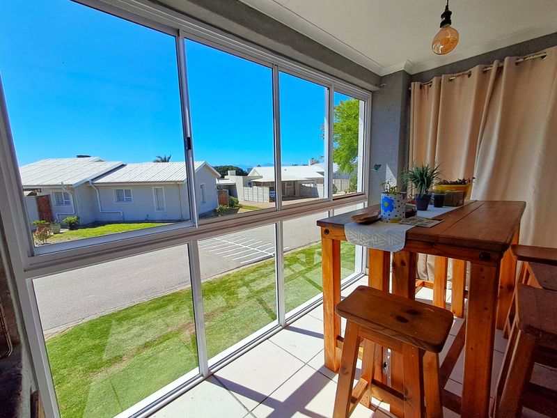 A bright, enclosed patio area featuring large sliding aluminium windows, tiled flooring, and a pendant light, offering a pleasant view of the street.