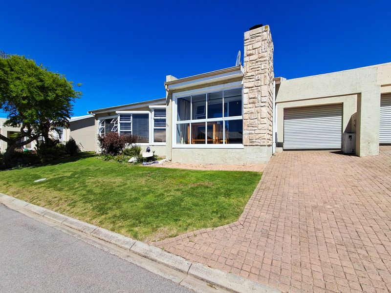 Front elevation of a single-story house featuring a paved driveway, garage, and a prominent stone-clad chimney with an enclosed sunroom.