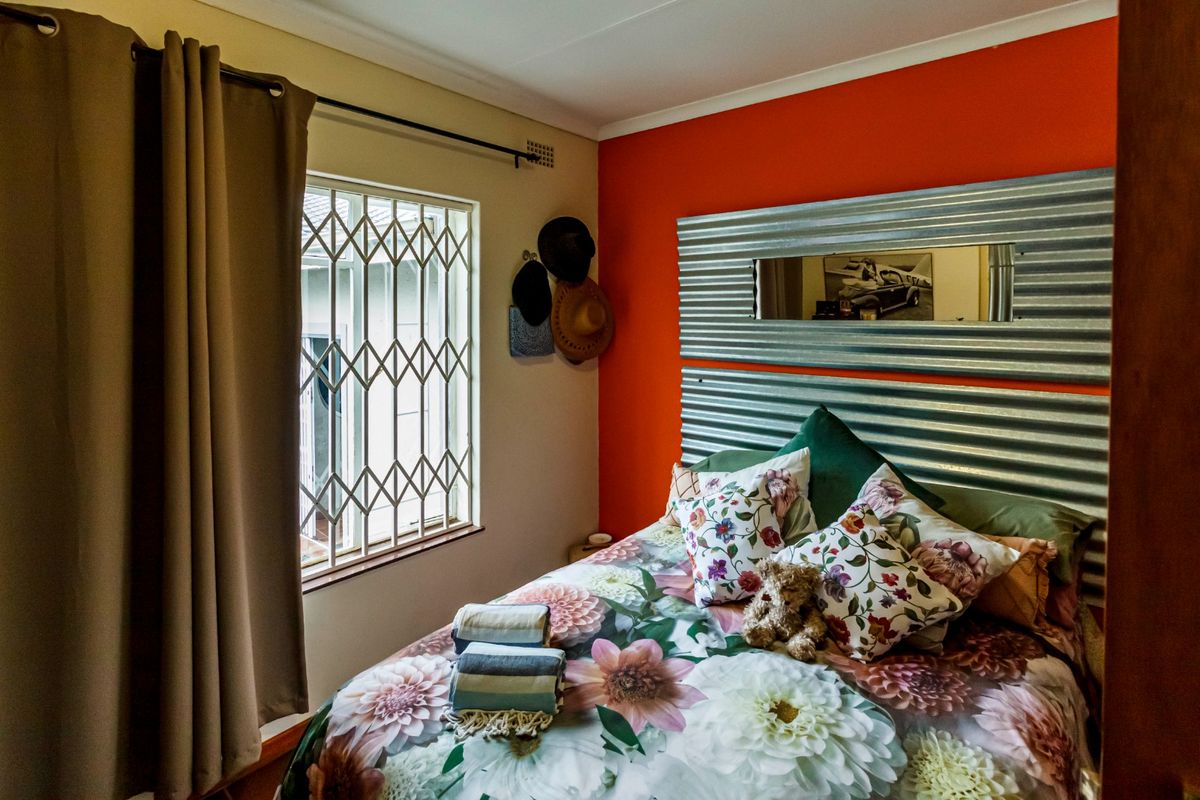 A bedroom featuring a bold orange accent wall, a unique corrugated metal headboard with an integrated mirror, and a window with a security gate.